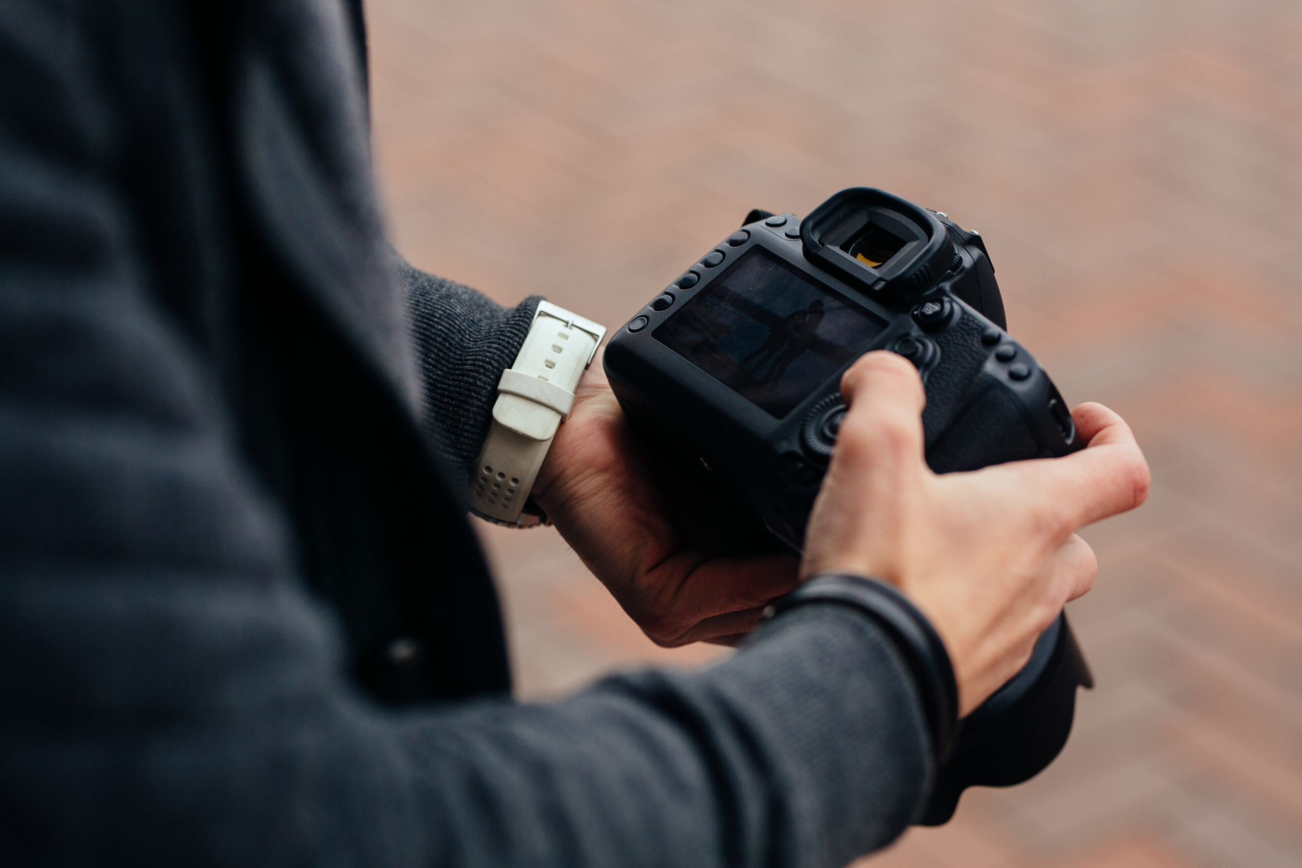 Photographer holding professional camera looks at photos, outdoors. Close-up.