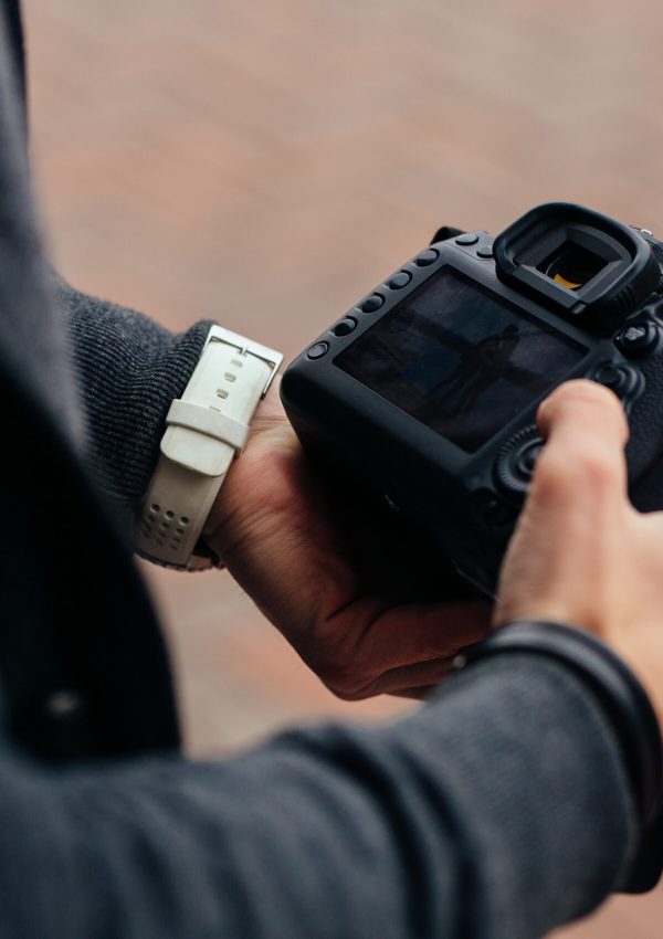 Photographer holding professional camera looks at photos, outdoors. Close-up.
